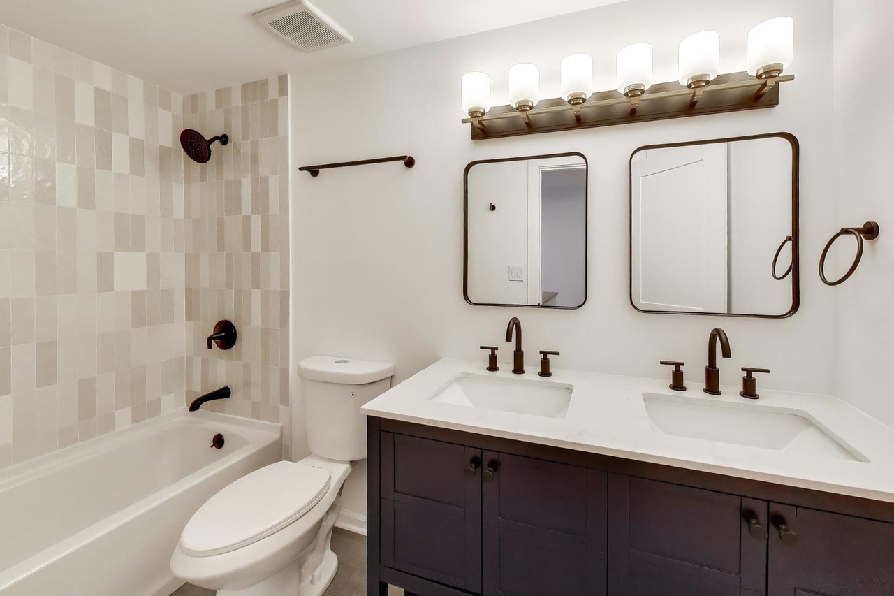 Renovated bathroom with double vanity and tiled tub surround